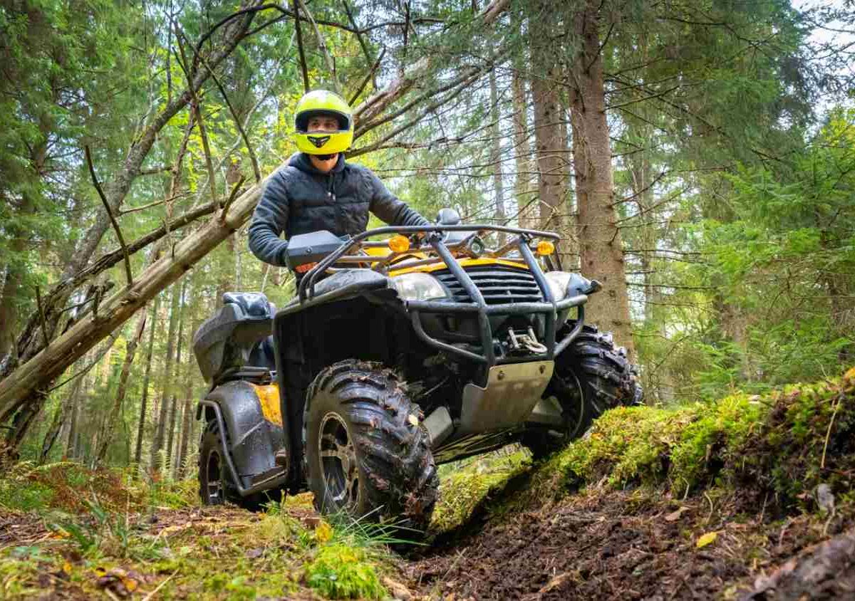 Adult ATV driver wearing a jacket and helmet in the forest.