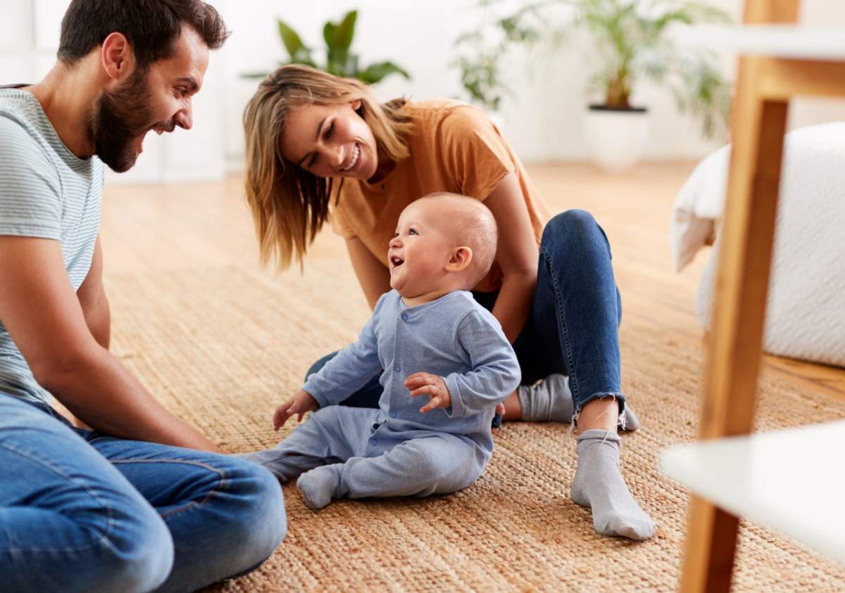 A family scene within a home living space including father, mother and child sitting on the floor laughing.