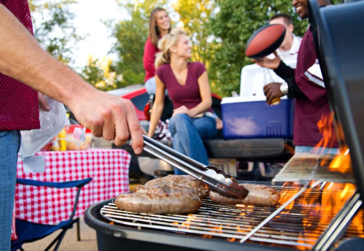 An ongoing outdoor BBQ scene with a manned grill and friends in the background talking.