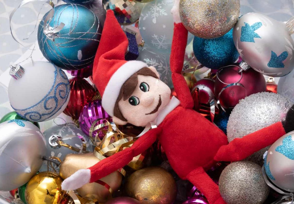 A Holiday-themed elf plush toy laying over a pile of Christmas tree ornaments.