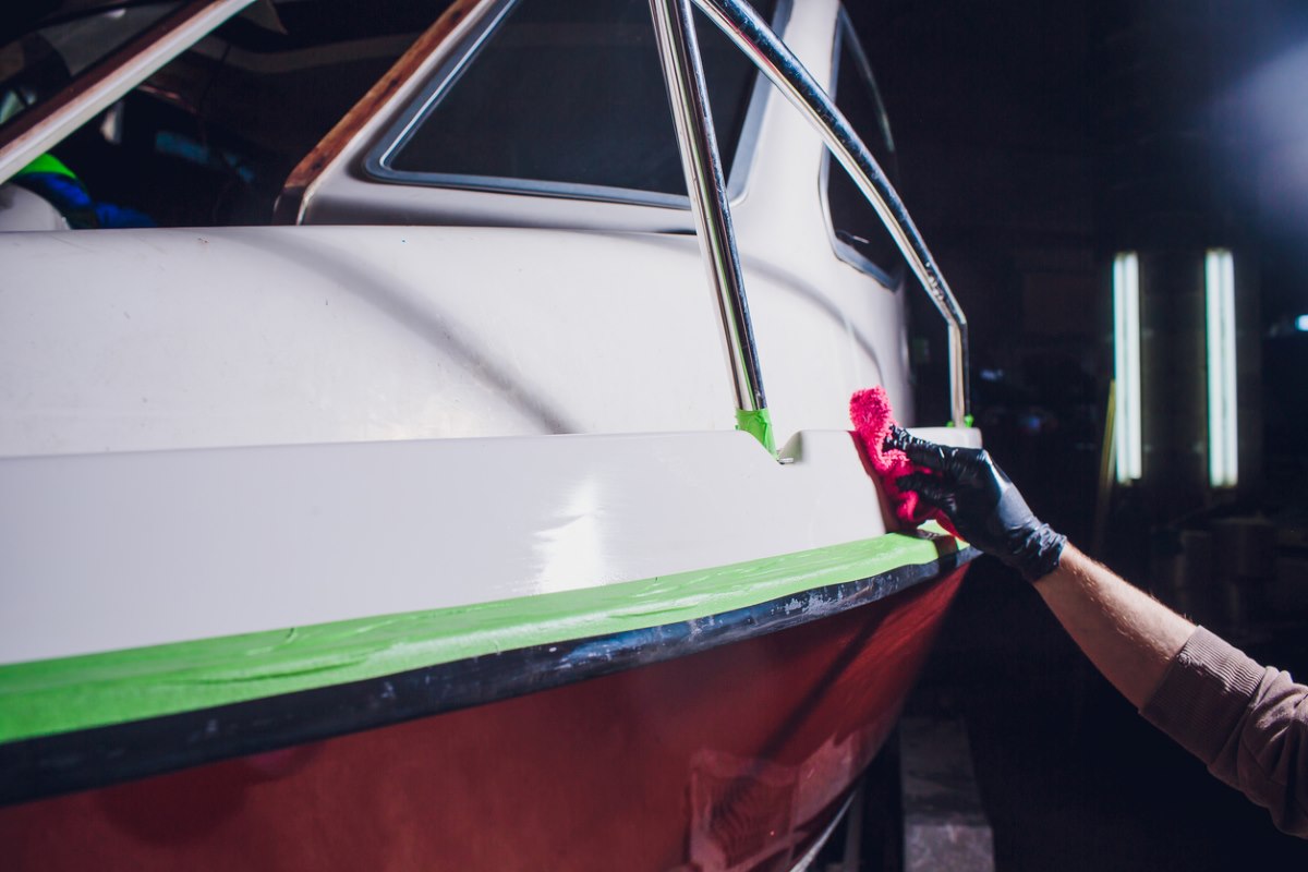 A person wipes the side of a boat with a pink rag.