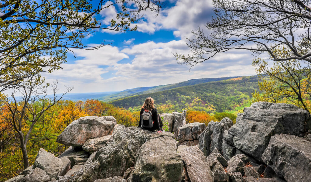 A young woman wearing a backpack gazes at the beautiful landscapes in the Blue Ridge Mountains.