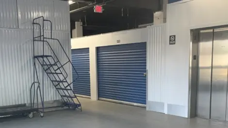 Indoor storage units with an elevator and a tall ladder next to wall.