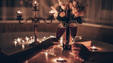 A couple toasts during a candlelit dinner with a bouquet of flowers on the table.