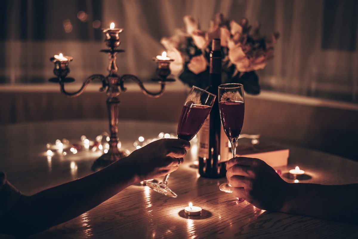 A couple toasts during a candlelit dinner with a bouquet of flowers on the table.