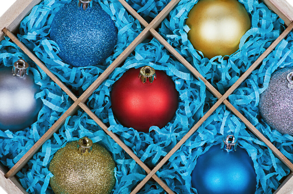 Colorful glass Christmas ornaments organized in a wooden box with blue tissue paper padding. 