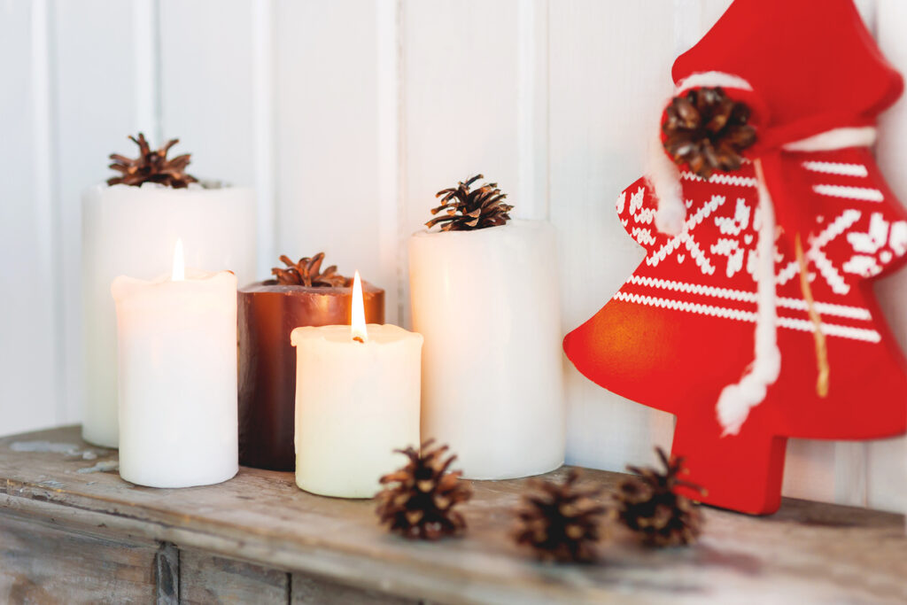 Scandinavian minimalist Christmas decorations on a wood surface with candles, pine cones, and a Nordic-print wood tree. 